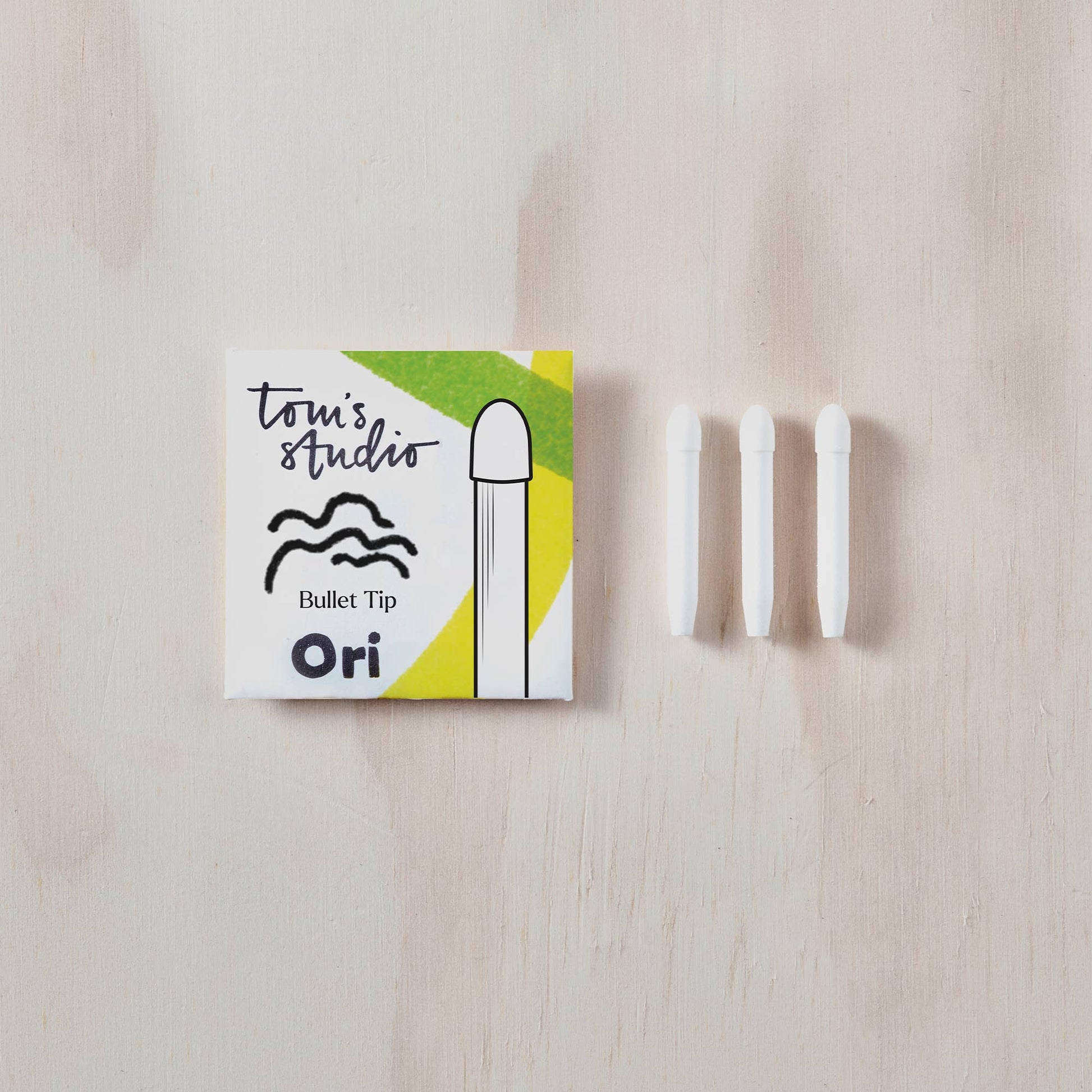Toni's Studio Ori bullet tip packaging with three white cylindrical items on a wooden surface
