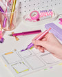 Person using a pink pen on a planner with stationery items in the background