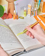 Person using a gold highlighter on an open book with a desk in the background