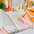 Person using a gold highlighter on an open book with a desk in the background
