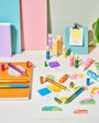 Colorful stationery items including markers, pens, and post-it notes on a white surface with a plant in the corner.