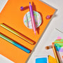 Colorful markers on an orange surface with a white background