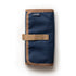 A partially unrolled tool roll with a brown waxed canvas exterior, aluminum hook fastener, and multiple pockets containing pens and other tools.