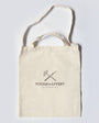 Beige tote bag with 'TOOLS TO LIVE BY' logo on a light gray background