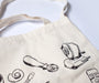 Canvas tote bag with black illustrations of stationery items on a white background