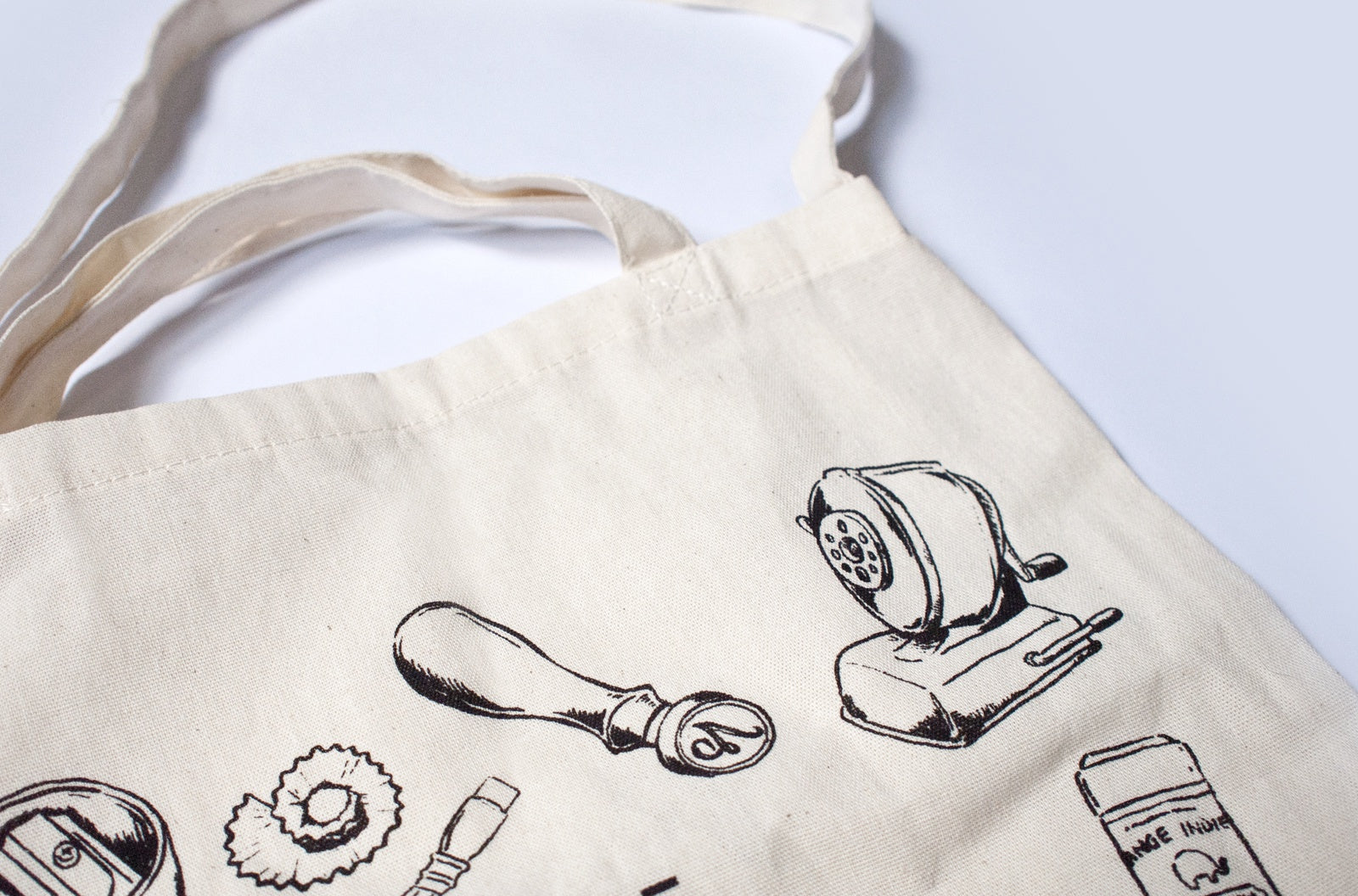 Canvas tote bag with black illustrations of stationery items on a white background