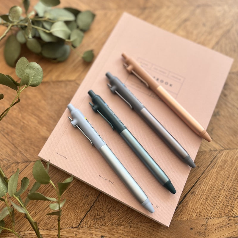 Set of pens on a notebook with greenery on a wooden surface
