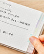 Hand holding a notebook with Japanese text on a wooden surface