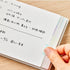 Hand holding a notebook with Japanese text on a wooden surface