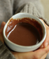 Person holding a small white bowl filled with a brown liquid, possibly hot chocolate.
