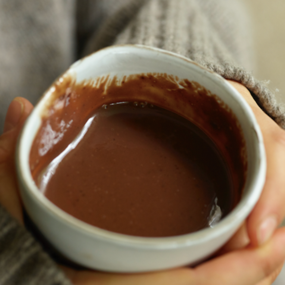 Person holding a small white bowl filled with a brown liquid, possibly hot chocolate.