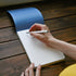 Person writing in a notebook on a wooden surface