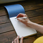 Person writing in a notebook on a wooden surface
