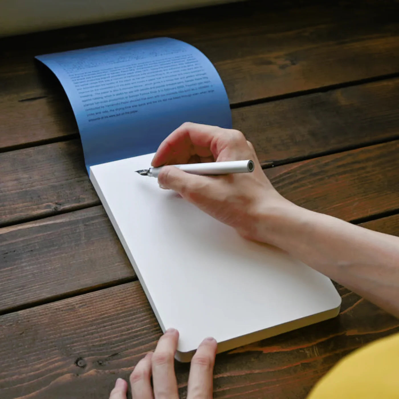 Person writing in a notebook on a wooden surface
