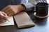 Person writing in a notebook with a black mug on a table