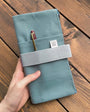 Teal fabric wallet with a pen held by a hand on a wooden surface
