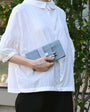 Person wearing a white shirt holding a gray clutch bag outdoors.