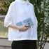 Person wearing a white shirt holding a gray clutch bag outdoors.
