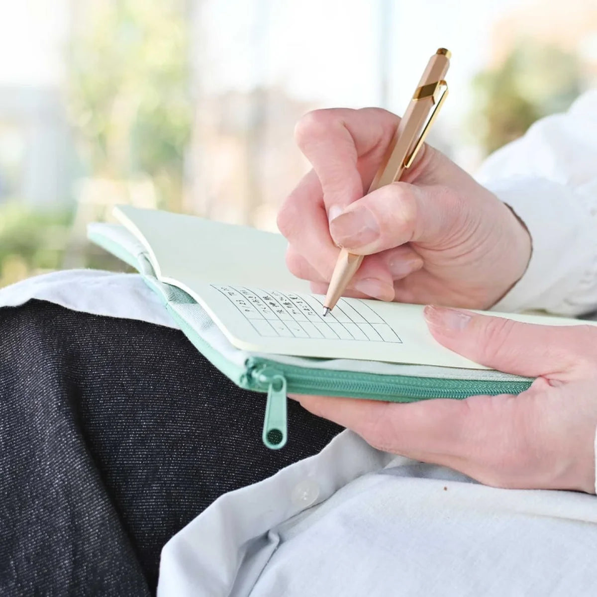 Person writing in a notebook with a pen outdoors