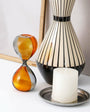 Decorative items including a striped vase, hourglass, and candle on a white surface.