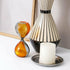 Decorative items including a striped vase, hourglass, and candle on a white surface.