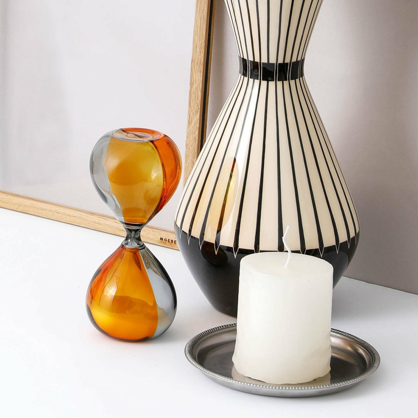 Decorative items including a striped vase, hourglass, and candle on a white surface.
