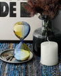 Decorative items including a glass hourglass, candle, and vase on a textured surface.
