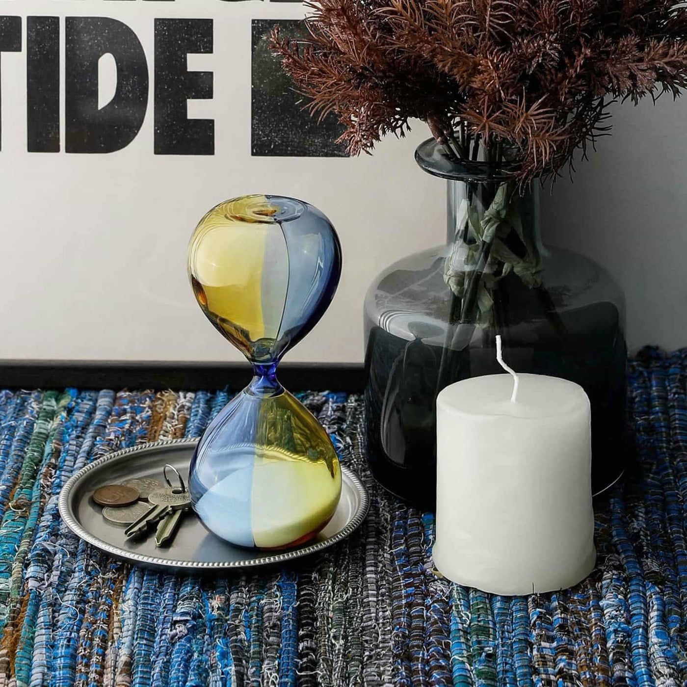Decorative items including a glass hourglass, candle, and vase on a textured surface.