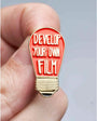 Light bulb-shaped pin with 'Develop Your Own Film' text held between fingers