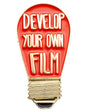 A light bulb-shaped enamel pin with a red body, gold metal outline and screw base, and raised cream lettering that reads 'DEVELOP YOUR OWN FILM' on a plain white background.