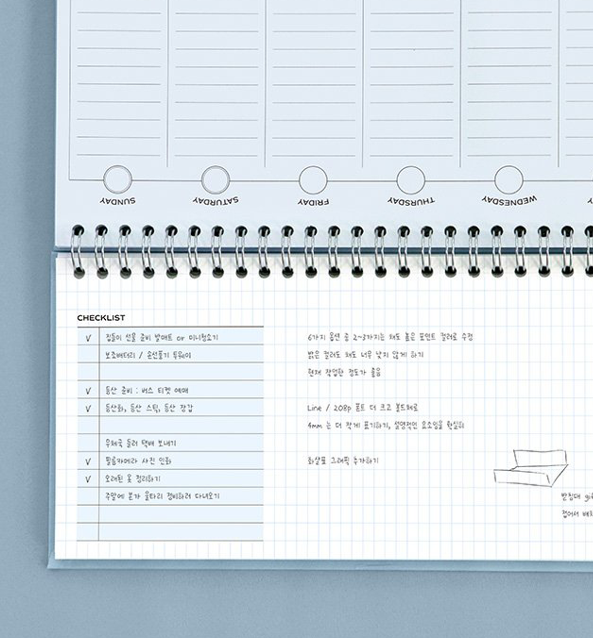 An open spiral-bound planner or notebook with Korean text, lined pages, weekly section headers, a checklist on the left page, and handwritten notes on the right, photographed against a light blue-gray background.