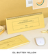 A butter yellow spiral-bound desk calendar and matching notepad displayed on a light beige desk with a white computer mouse, a gold pen, and a small stack of books. The text 'O1.