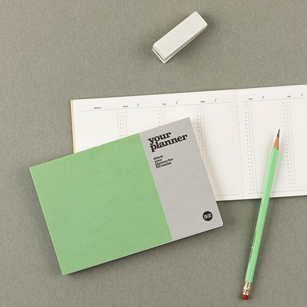 Green planner with a gray cover, pencil, and eraser on a gray surface