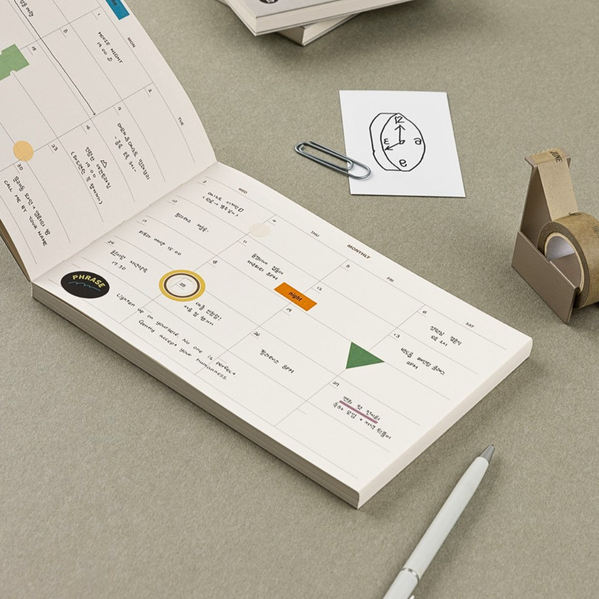 Open planner with colorful icons on a beige surface with a pen and paper clip.