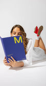 Woman reading a blue book with a yellow 'M' on a white background