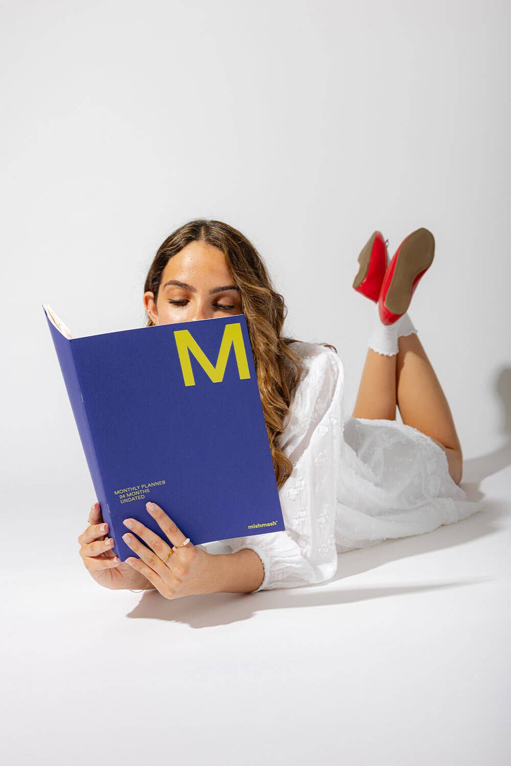 Woman reading a blue book with a yellow 'M' on a white background