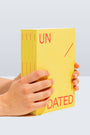 Yellow book titled 'UNDATED' held by a hand on a light gray background