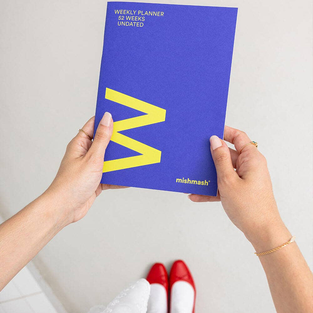 Person holding a blue planner with a yellow 'M' on a white background