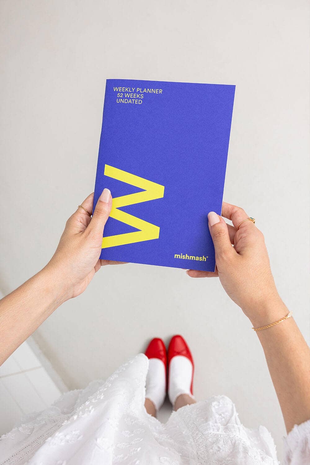 Person holding a blue planner with a yellow 'M' on a white background