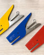 A set of four handheld staplers in red, blue, yellow, and silver colors, laid out on a surface.